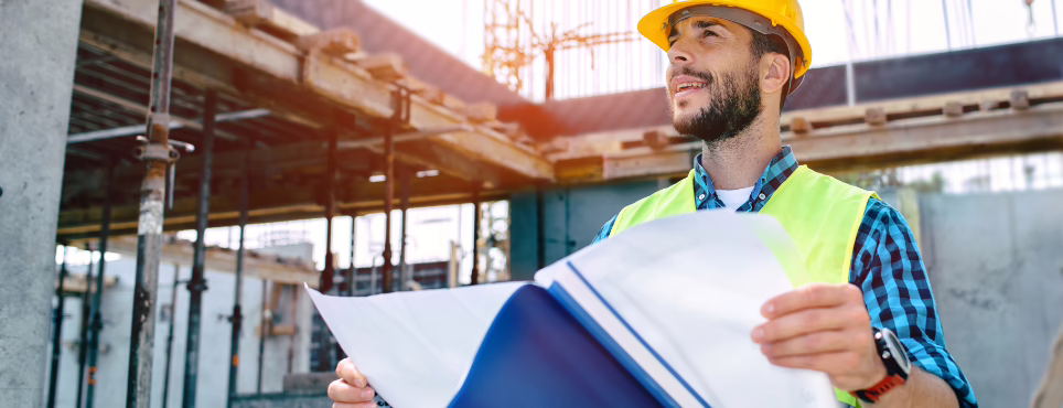Ingeniero civil con casco y chaleco revisando planos en una obra en construcción